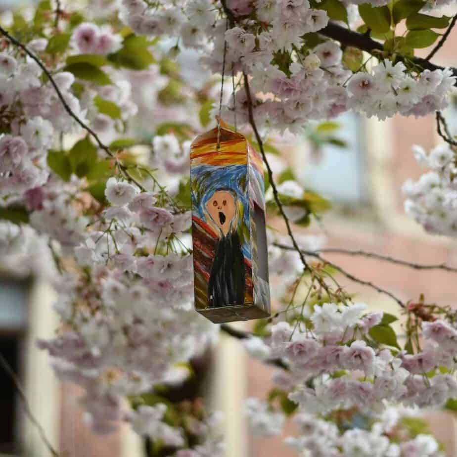 Ein nach dem Bild "Der Schrei" von Munch bemalter Milchkarton hängt in einem blühenden Baum