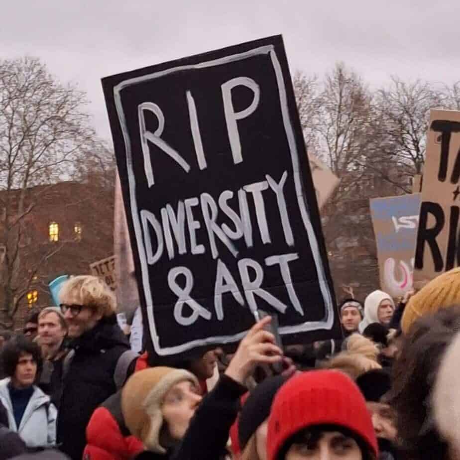 Ein Plakat wird auf einer Demonstration in die Höhe gehalten, darauf steht RIP DIVERSITY & ART